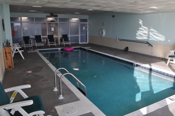 An indoor swimming pool with clear water, a lifeguard chair, and a pool ladder.