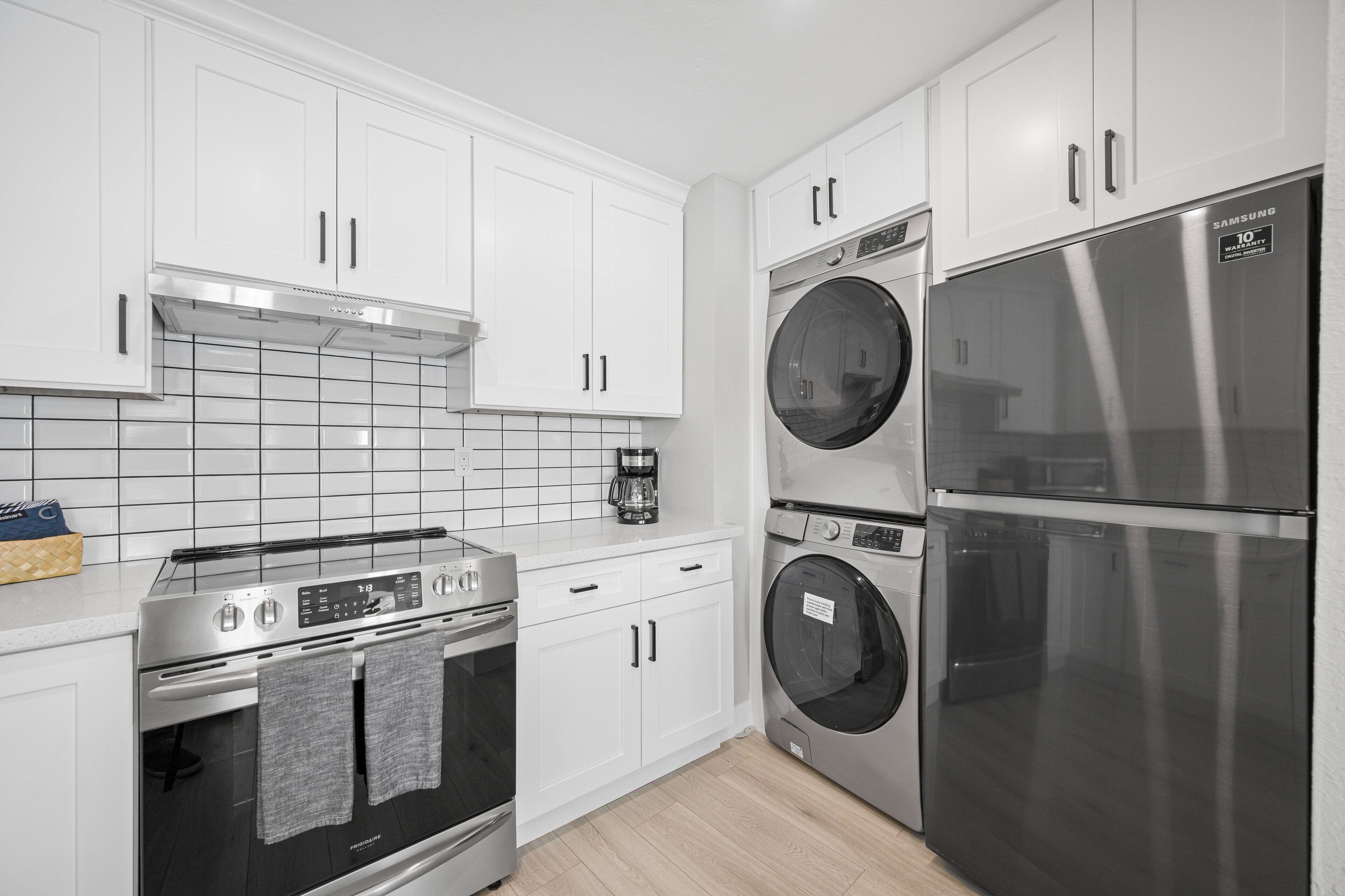 A modern kitchen with white cabinets, a stainless steel oven, a washing machine, and a refrigerator.