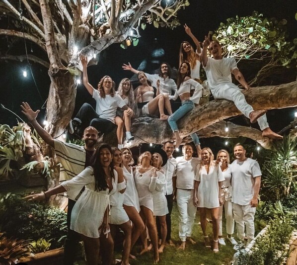 Un groupe de personnes vêtues de blanc posent sous un arbre décoré de guirlandes lumineuses.