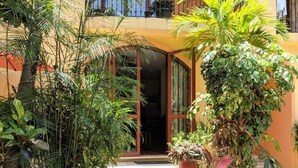 A two-story building with a covered patio area, surrounded by lush tropical plants and a small garden. - GEM w Pool near BEACHes & 5th Ave. Hi-speed Wifi, Top-Notch  LOCATION. KIDs OK! (Playa del Carmen)