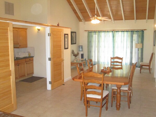 A spacious dining area with a wooden table and chairs, a kitchen with wooden cabinets, and a ceiling fan.