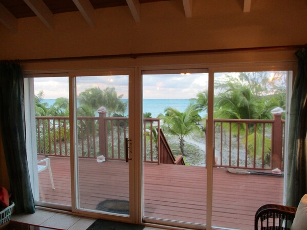 A room with a sliding glass door leading to a balcony with a view of the beach and ocean.