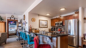 Een moderne keuken met een centraal kookeiland, roestvrijstalen apparatuur en een zithoek met barkrukken.