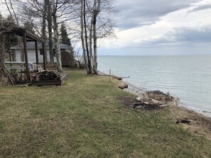 Un chalet au bord du lac, doté d’une terrasse, d’un foyer et d’une pile de bois de chauffage.