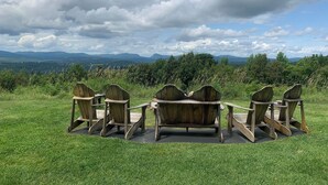 Filea di poltrone in legno di tipo Adirondack rivolte verso un panorama montuoso e un cielo nuvoloso.