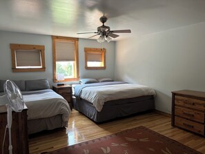 A bedroom with two beds, a ceiling fan, and wooden flooring.