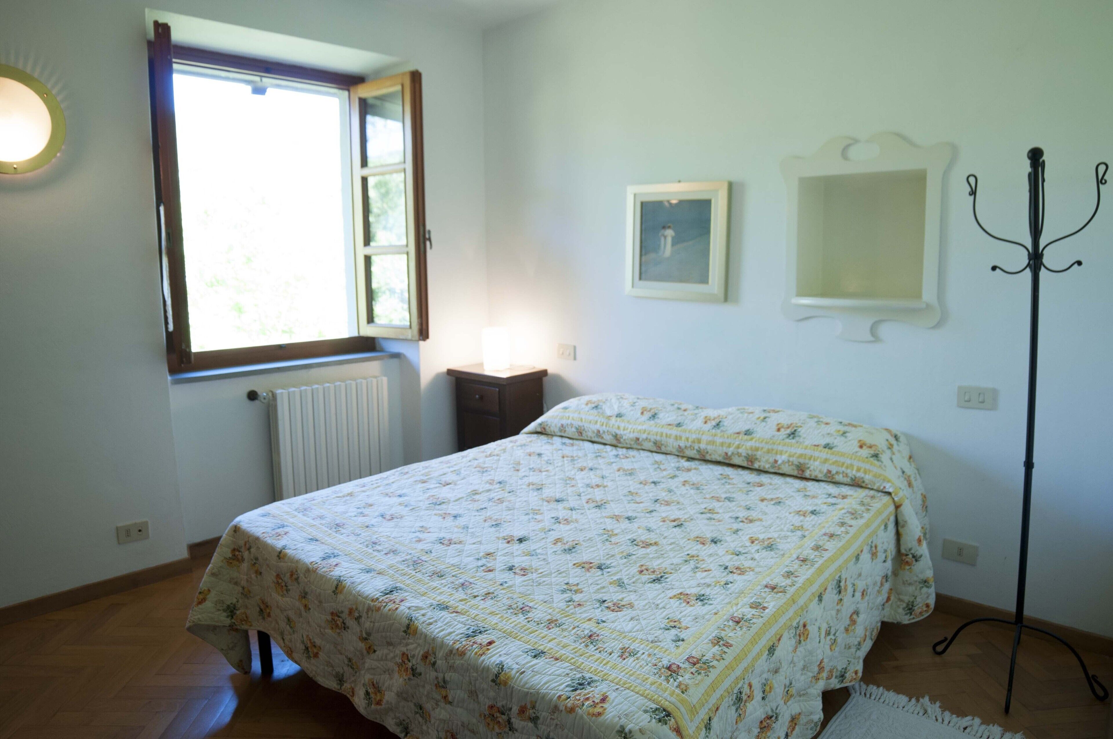A bedroom with a bed, a window, a radiator, and a coat rack.