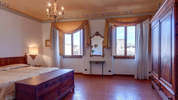 Ein Schlafzimmer mit einem hölzernen Bett, einer Kronleuchter, einem großen Spiegel und Blick auf die Stadt durch die Fenster.