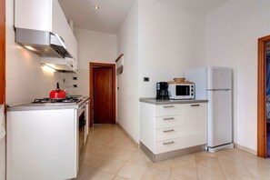 A compact kitchen with white cabinets, a gas stove, a microwave, and a refrigerator. - 3 bedrooms apartment close to Pitti Palace (Florence)