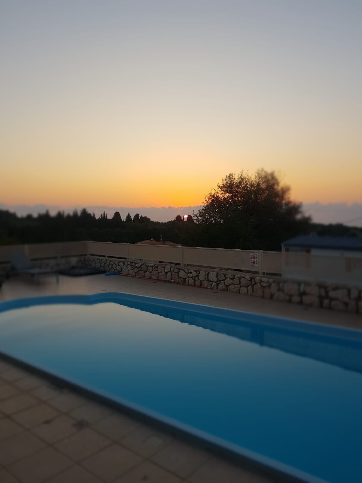 Una piscina con un muro de piedra y vistas al atardecer.