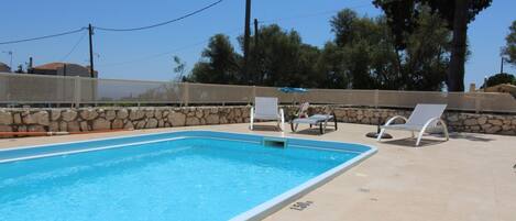 Une piscine avec des chaises longues et un mur en pierre.