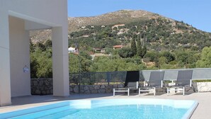 En swimmingpool med solstolar och utsikt över en sluttning med hus.