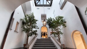 A grand staircase with ornate railings, flanked by trees and leading to a brightly lit interior space.