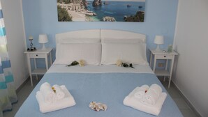 Ein Hotelzimmer mit einem großen Bett, zwei Nachttischen, einem Gemälde mit einer Küstenansicht und zwei Handtüchern auf dem Bett.
