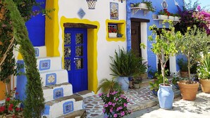 Ein Gebäude im traditionellen mediterranen Stil mit einer blauen Tür, gelben Akzenten und Blumentöpfen.