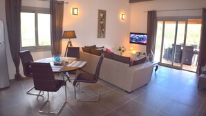 Ein modernes Wohnzimmer mit einer Couch, Sesseln, einem Esstisch und einem Fernseher.