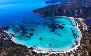 Vue aérienne d’une zone côtière avec des eaux turquoise limpides, une plage de sable et une petite île couverte d’une végétation luxuriante.