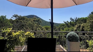 Ein Balkon mit einem beige-farbenen Sonnenschirm, Blick auf einen Berg und einem Blumentopf.