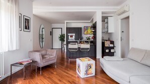 A modern living room with a sofa, a coffee table, and a dining area with chairs and a kitchen in the background.