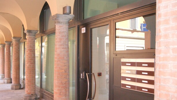A hallway with brick columns, a glass door with a keypad, and a tiled floor.