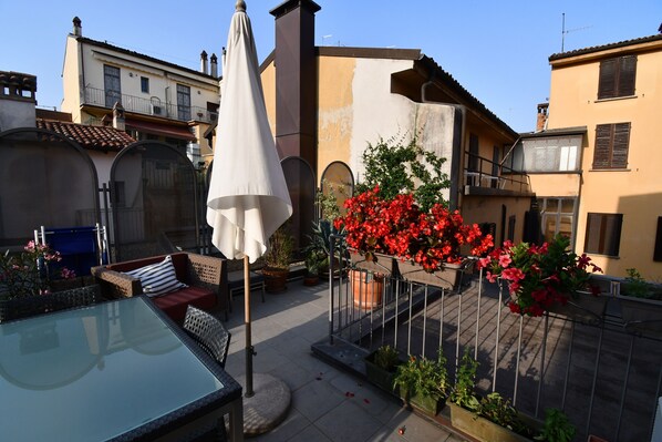 A courtyard with a glass table, outdoor seating, and red flowers.