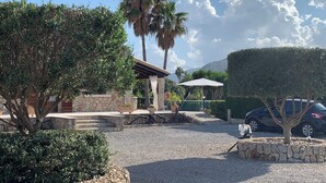 A courtyard with a stone wall, a pergola, palm trees, and a car parked nearby. -  VILLA CAN TOMI quiet farm house, private parking, wifi, gardens. (pollensa)