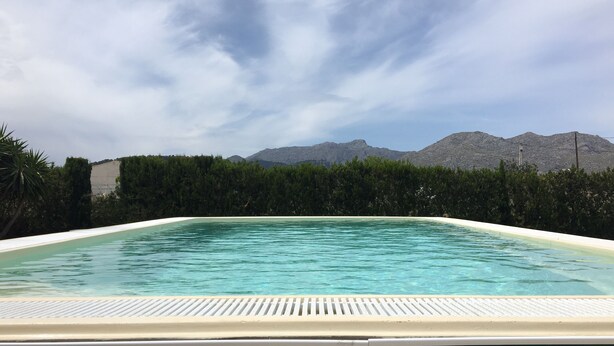 A rectangular swimming pool with a white edge, surrounded by green hedges and a mountain backdrop. -  VILLA CAN TOMI quiet farm house, private parking, wifi, gardens. (pollensa)