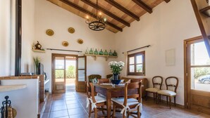 A spacious dining area with a wooden table and chairs, a chandelier, and a view of the outdoors through large windows. -  VILLA CAN TOMI quiet farm house, private parking, wifi, gardens. (pollensa)