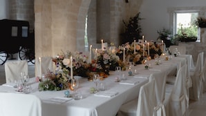 Une longue table de banquet, dressée pour un événement formel, avec des nappes blanches, des bougies et des compositions florales.