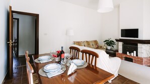 A dining area with a wooden table set for four, a sofa, a TV, and a fireplace. - Villa del Concho and Syracuse (Plemmirio)