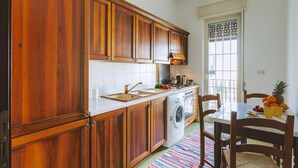A kitchen with wooden cabinets, a washing machine, a dining table with chairs, and a window with a view. - Villa del Concho and Syracuse (Plemmirio)