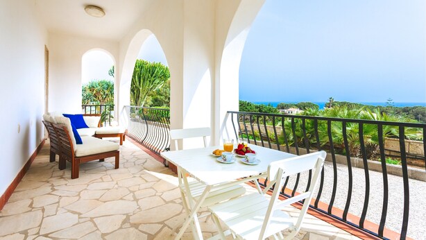 A balcony with white furniture, a table with a drink and fruit, and a view of the sea. - Villa del Concho and Syracuse (Plemmirio)