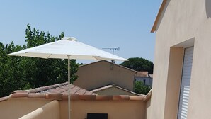A rooftop terrace with a white umbrella, black wicker furniture, and a pink metal table and chair.