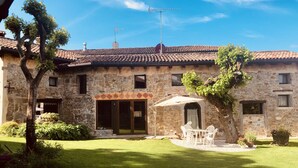 Un edificio in pietra con tetto in tegole, un patio coperto con mobili da esterno e un prato ben curato.