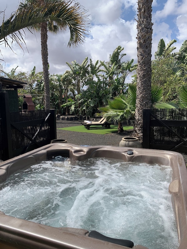 A hot tub surrounded by lush tropical plants and a fenced area with lounge chairs. - Cozy Villa in Lajares with private jacuzzi and garden, offers in September. (Lajares)