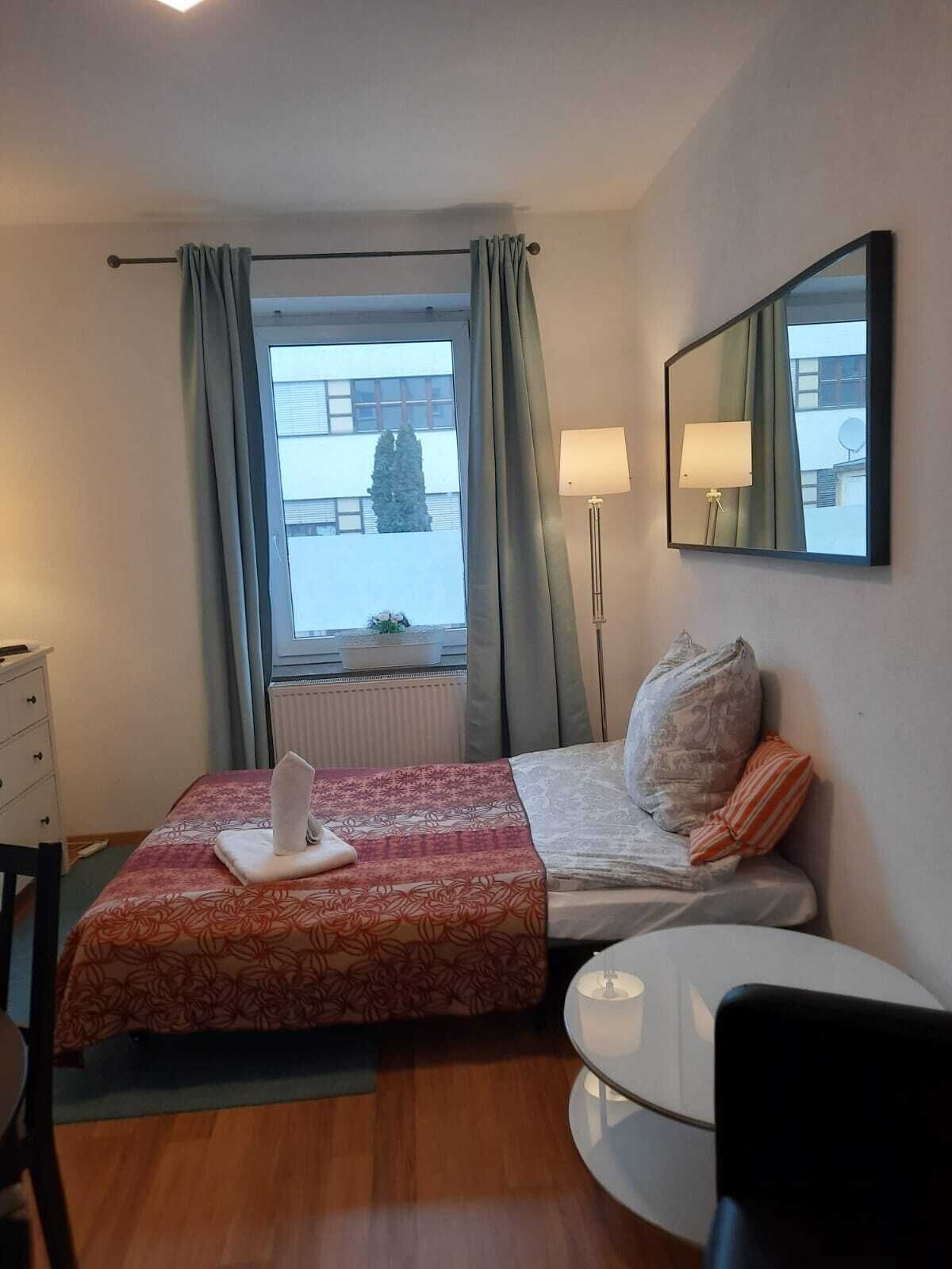 A hotel room with a bed, a bedside table, a chair, a lamp, and a window with curtains.