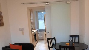 Un espacio habitable compacto con comedor, cocina al fondo y una pequeña zona de estar con sofá y mesa.