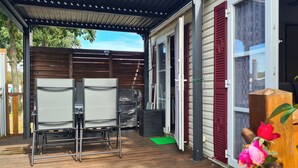 Ein überdachter Patio-Bereich mit zwei Stühlen, einem kleinen Tisch und einer grünen Matte.