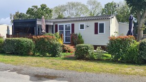 Ein Bungalow mit einer Veranda, einem kleinen Garten und einem gepflasterten Auffahrt.
