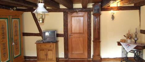A traditional room with wooden beams, a wooden door, a television on a cabinet, a sewing machine, and a patterned rug.