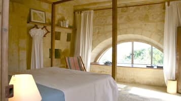 Relax in a traditional room with a four-poster bed, stone wall, and arched window.