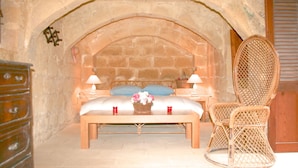 A bedroom with a stone arch, a bed with white linens, two bedside lamps, a wicker chair, and a small table with a vase of flowers. - CALM - ZENITUDE - ONE OF THE MOST BEAUTIFUL HOUSES OF GOZO (GHARB)