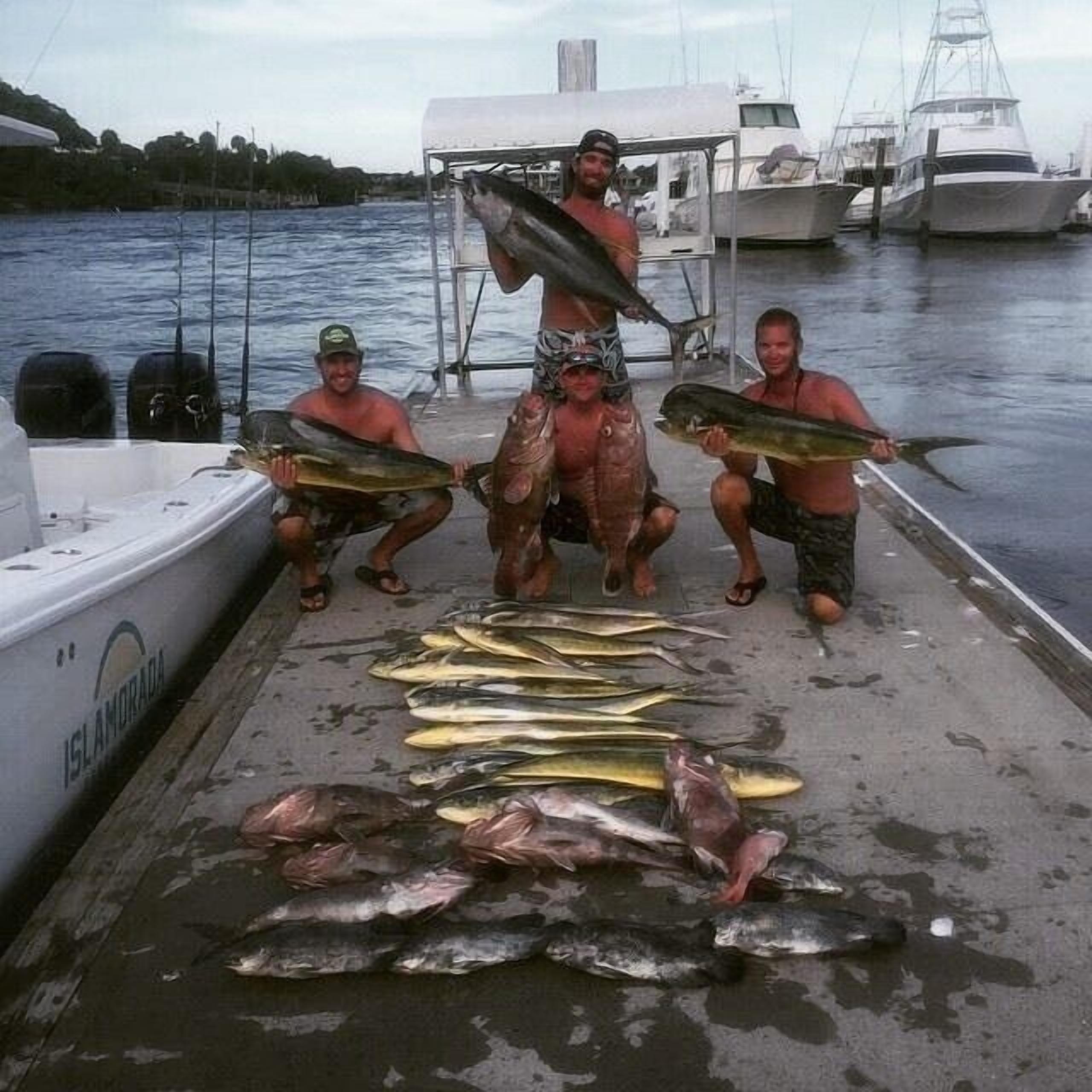 En båt låg förtöjd vid en småbåtshamn, och flera personer stod där och höll i fiskar.