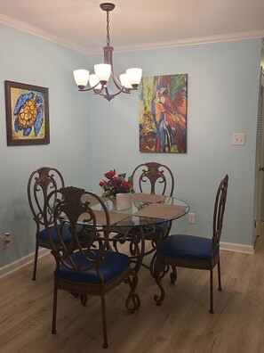 A dining area with a round glass table, four ornate chairs, and a chandelier. - Beautiful Condo Steps to the Gulf!  (Gulf Shores)