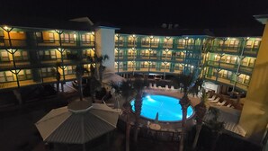 A multi-story hotel with a central swimming pool surrounded by lounge areas and palm trees. - Beautiful Condo Steps to the Gulf!  (Gulf Shores)