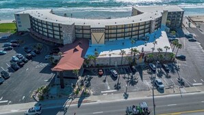 Un hotel costero con estructura curva, estacionamiento y vista al océano.