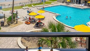 Zona de piscina con vista a la playa, sillas de descanso, sombrillas y una torre de socorristas.