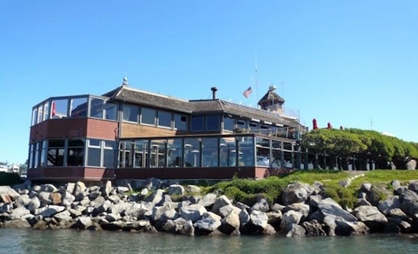 Un bâtiment situé au bord de l’eau, doté d’une façade en verre, d’une partie en briques rouges et d’un mât pour drapeau.