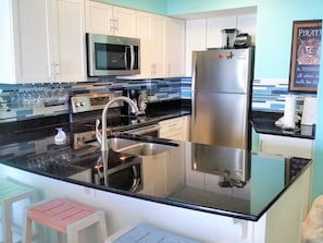 A modern kitchen with stainless steel appliances, a black countertop, and white cabinetry.