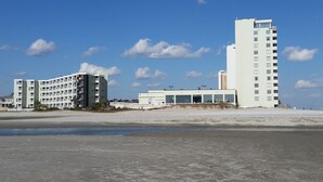 Un hotel frente a la playa con varias construcciones, incluyendo una torre blanca alta y un edificio más bajo con balcones.